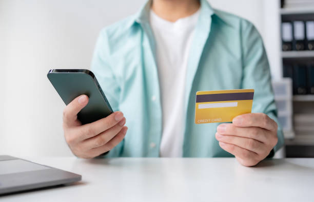 istock Man making financial transaction using credit card and smartphone. Young man paying online, using banking service, entering information, shopping, ordering in internet store, doing secure payment. 2155122755