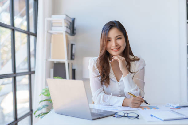 istock Professional asian businesswoman with a confident smile in a bright office setting with a laptop and documents. 2155123072