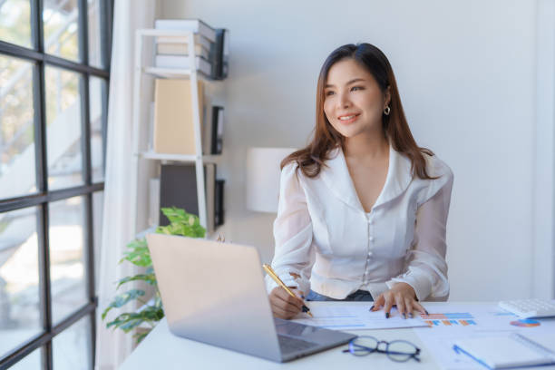 istock Professional asian businesswoman with a confident smile in a bright office setting with a laptop and documents. 2155123091