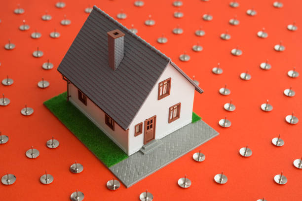 Modern house in many danger thumbtacks pins on red background. Mortgage loan for buying home or real estate property, money risk management planning in financial, foreclosure and bankruptcy concept.