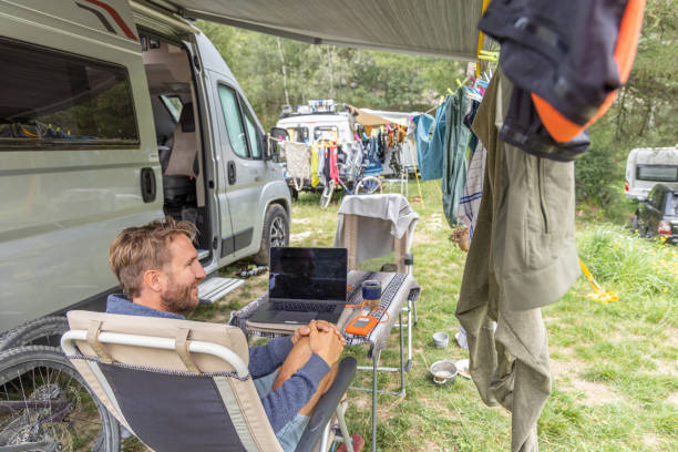 istock Man Working on Laptop at Campsite with Camper Van and Drying Clothes 2155136484