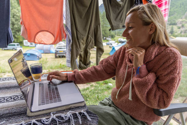 istock Woman Smiling While Working on Laptop at Campsite with Drying Clothes 2155136537