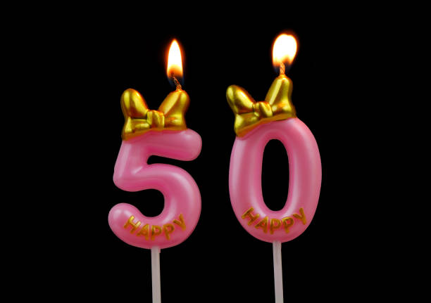 Pink birthday candles with bow burning on black background, number 50.