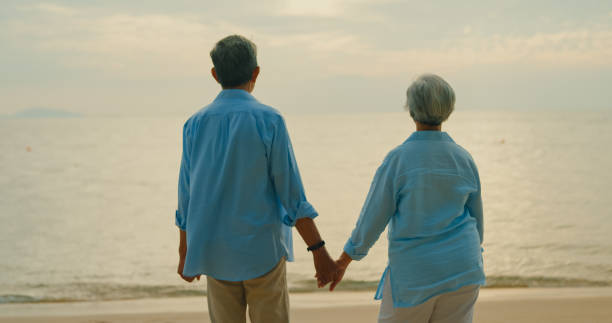 istock Asian elderly cheerful couple holding each other hand and smiling looking at camera on beach enjoying the sea view. A happy senior adult people enjoy the travel lifestyle after retirement. 2155144754