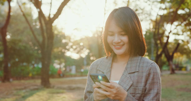 istock A young Asian businesswoman smiling while looking at her smartphone, possibly reading good news, in an urban park setting. Sustainable business outdoor. 2155145439