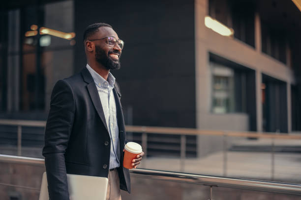 African businessman outdoors holding laptop and take away coffee cup