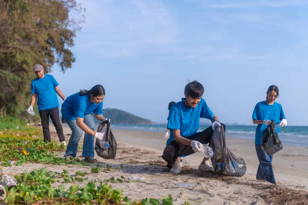 istock Plastic pollution and environmental problem concept. Happy asian diverse group of volunteers with garbage bags wearing blue t-shirt and cleaning plastic on the beach. Volunteers collecting trash. 2155151145