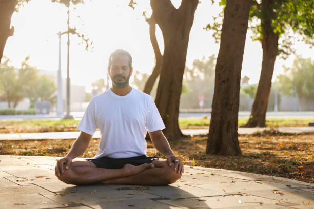 istock Indian man sitting cross-legged on ground in public park and practicing yoga 2155154190