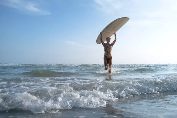 Surfer woman holding surf board coming out from the sea.