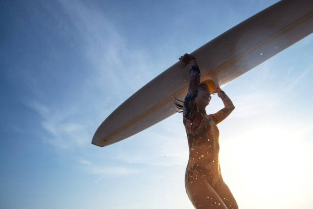 Female surfer wearing a swimsuit holding a surfboard on her head, running towards the waves is fun in an extreme water sport, makes splashes, view from below