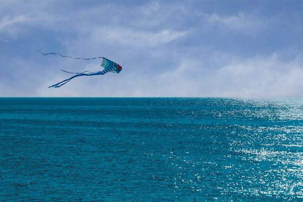 A kite is flying over Lake Michigan. The sky is cloudy and the water is calm. The kite is white and blue