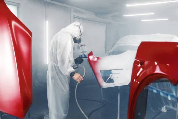 istock Car paint worker spraying red paint to car body element using spray gun in vehicle workshop chamber. Complex restoration of automobile body. 2155165687