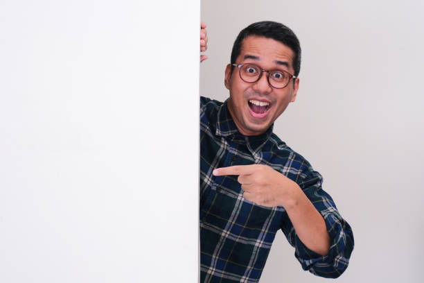 istock A man peeking behind white billboard showing amazed expression and pointing on it 2155168470