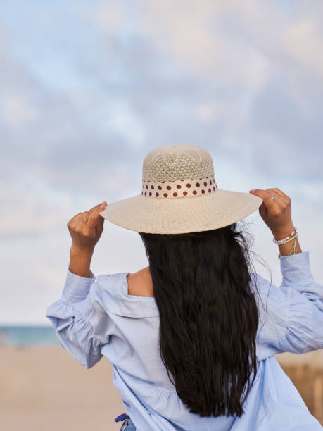 A woman wearing a straw hat stands on a beach