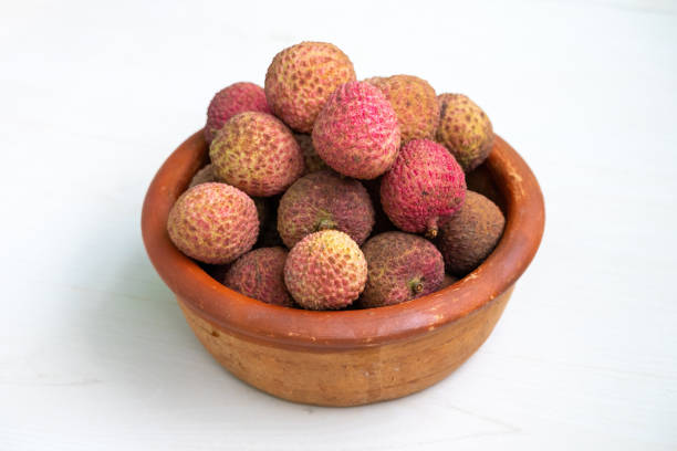 Collection of lychee fruits in green bowl showcasing their vibrant red skins juicy white flesh and large central seeds. Perfect for concepts of tropical fruits, fresh produce, or culinary ingredients.