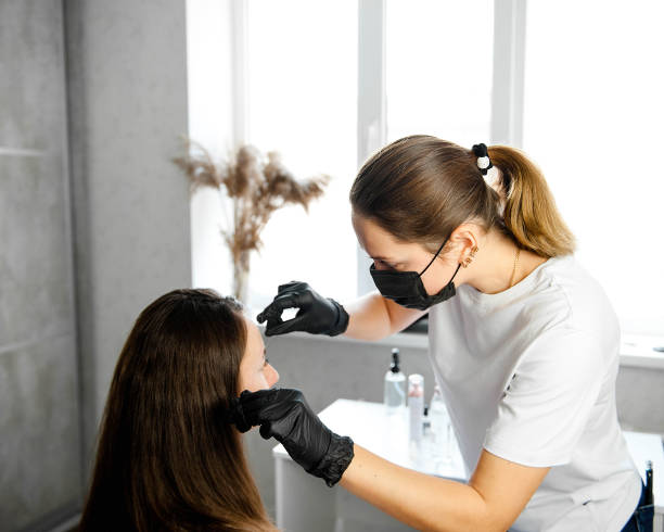 istock Browist makes eyebrow correction with tweezers. A model with dark hair in a light studio is sitting on an eyebrow correction at the eyebrow master. 2155180732