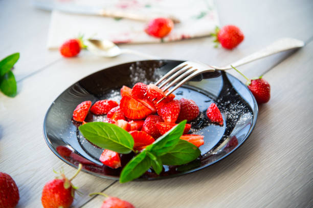 fresh fruit salad of ripe strawberries on a light wooden table .