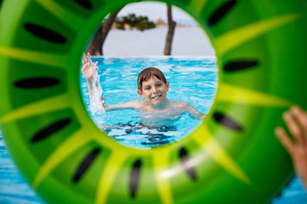 A young boy having fun swimming in the sea, partially submerged, using a bright green inflatable ring on a sunny day.