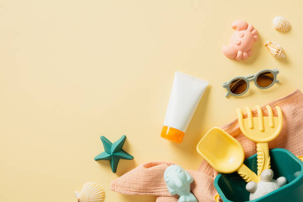 istock Summer Beach Essentials Flat Lay. Top view sunscreen tube, sand molds, bucket with rake and shovel, stylish baby sunglasses on yellow background. 2155207180