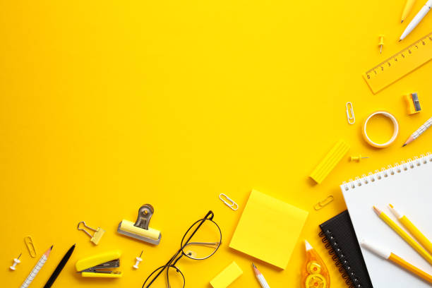 istock Flat lay composition with office supplies. Top view pencils, pens, paper clips, eyeglasses, a notebook, and other desk accessories on yellow background 2155207905