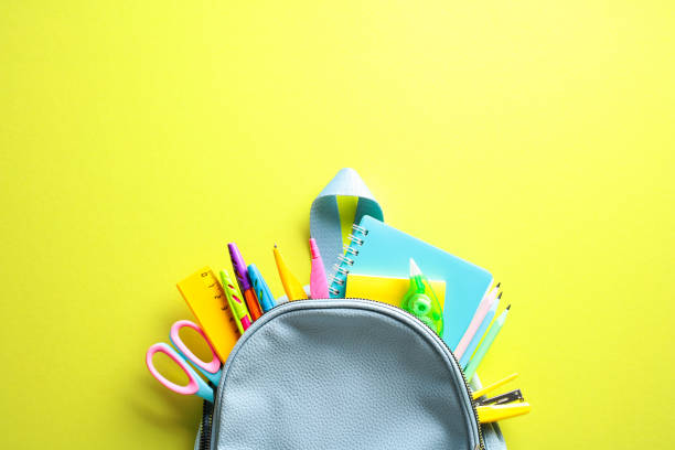 istock Back to school concept with vibrant school supplies spilling from a backpack on a yellow background 2155208405