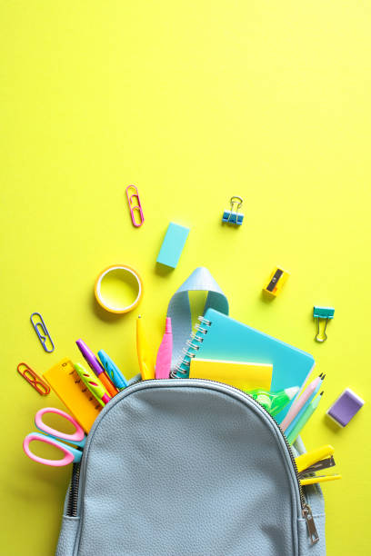 istock Back to school concept with vibrant stationery spilling from an open backpack on a yellow background 2155208480
