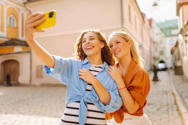istock Two young smiling women in summer clothes taking selfie self portrait photos on smartphone. 2155208564
