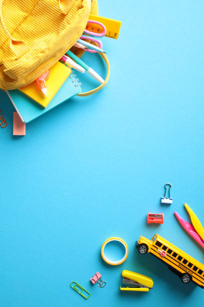 istock Back to school concept with colorful stationery and a yellow backpack on a blue background. Flat lay, top view, vertical. 2155208654
