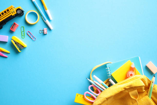 istock Back to school concept with school supplies scattered on a vibrant blue background. The image features a yellow backpack, notebooks, pens, pencils, scissors, rulers, and various colorful clips 2155208738