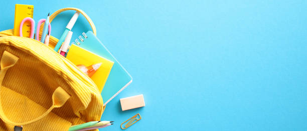istock Back to School Concept. Brightly colored yellow backpack overflowing with essential school supplies on a vivid blue background. Flat lay, top view, copy space. 2155208795