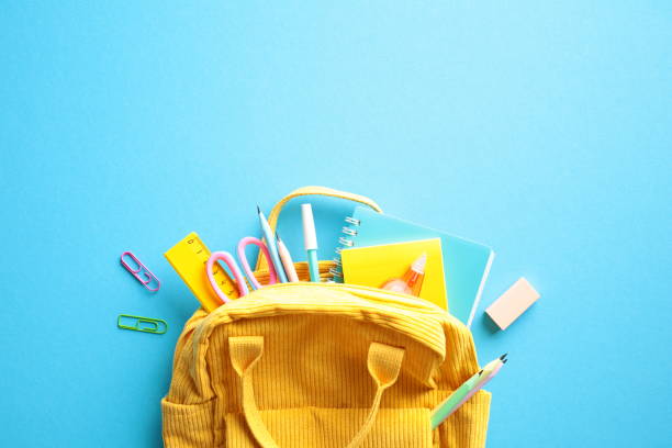istock Back to School Concept. Brightly colored yellow backpack overflowing with essential school supplies such as notebooks, pens, pencils, scissors, and a ruler on a vibrant blue background. Flat lay. 2155208818
