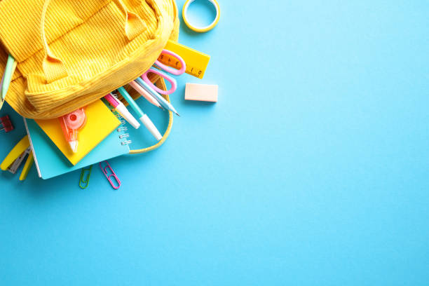 istock Colorful Back to School Concept. Yellow backpack with various school supplies, including pencils, scissors, an eraser, paper clips, and a ruler on light blue background. Flat lay, top view. 2155209479