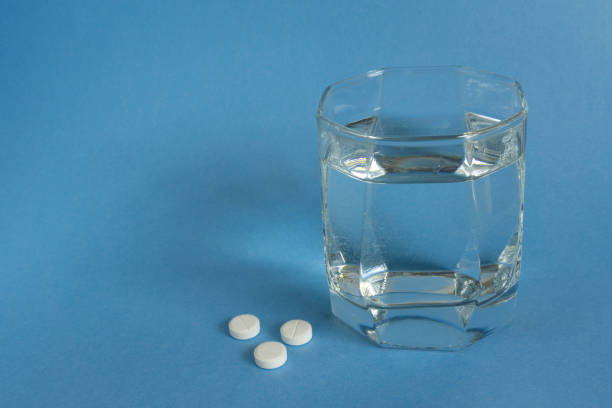 istock Three pills or tablets with glass of water on blue background 2155209821