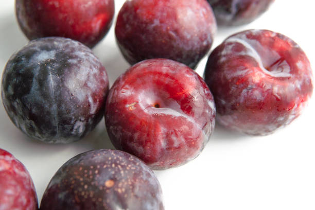 A close-up photograph of a cluster of fresh red plums \nwith dewdrops, showcasing their vibrant colors and natural textures. The plums are arranged on a white surface with soft shadows in the background, emphasizing their juicy and appetizing appearance. This image is perfect for use in food photography, advertising, and editorial content, capturing the essence of fresh, organic fruit.
