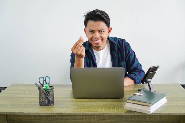 istock young asian businessman sitting at workplace doing money gesture 2155232666
