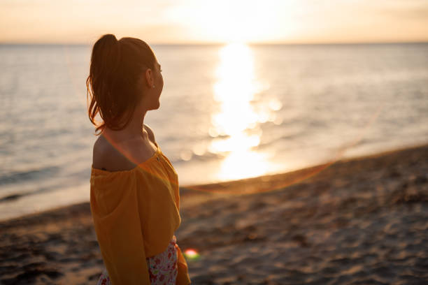 istock Young woman enjoying sunset by the sea 2155243938