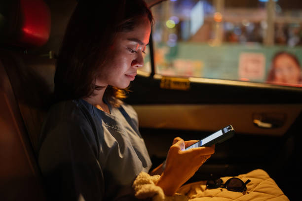 Mid-adult nurse is using her phone while coming back home from work with a taxi.