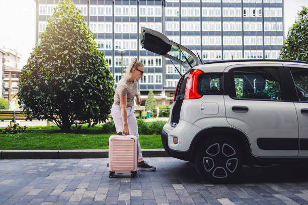 istock Woman loading suitcase into car trunk on city street 2155261882