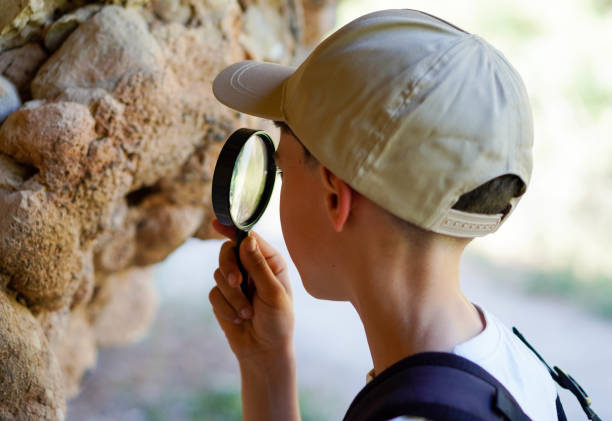 istock boy with backpack cap and magnifying glass, looking closely at the living creatures that inhabit a rock face 2155262598