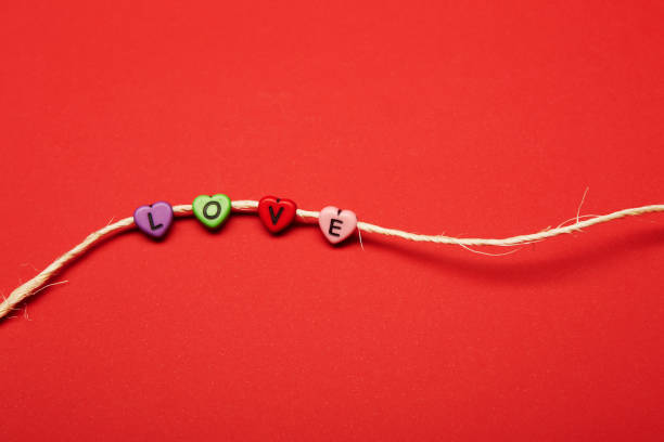Colored heart shaped beads with letters on them strung on a white country style rustic rope making Love word on the bright solid fond plain red background