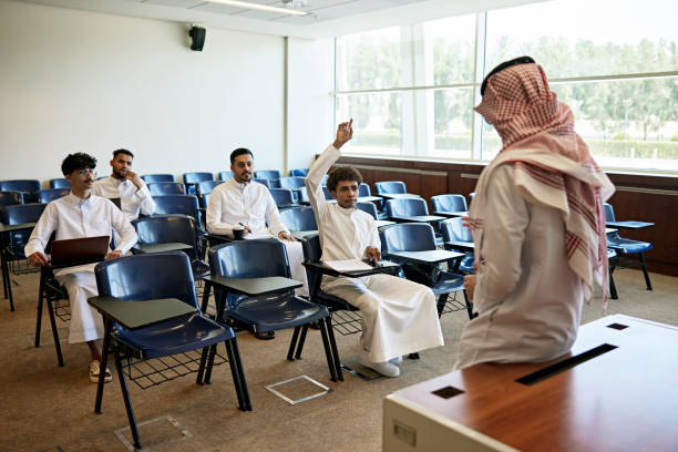 istock Young male student answering to teacher while sitting on chair during lecture in classroom 2155267286