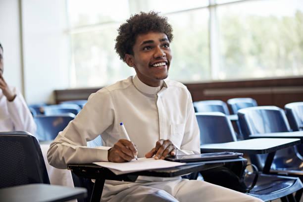 istock Smiling young male student looking away while sitting on chair in classroom 2155267307