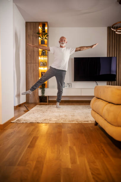 istock A senior man is standing at home on on foot and practicing yoga. 2155276948