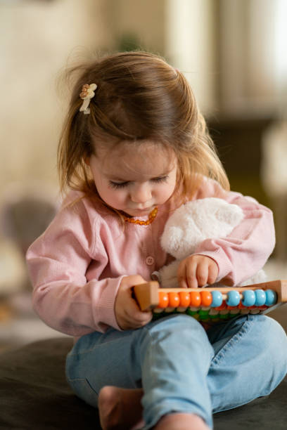 Cute little girl holding teddy bear and playing whit abacus at home
