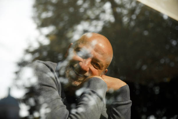 istock Cheerful senior man with a beard leaning on his hands and smiling through a window 2155278136