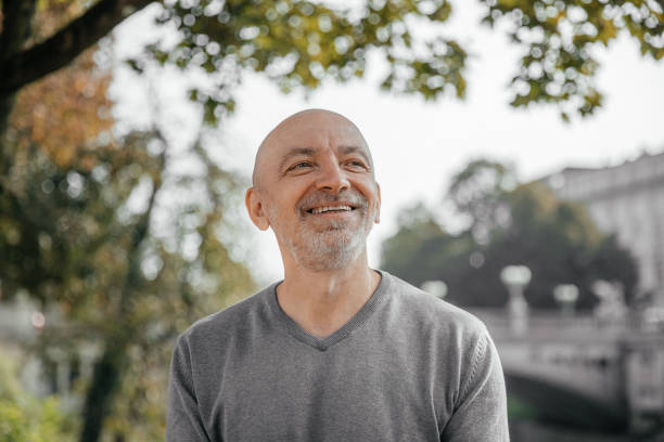 Elderly man smiling warmly while sitting in a park, trees and river in background