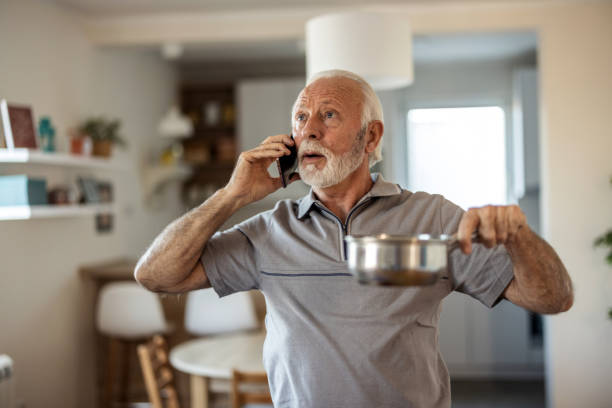 istock Worried senior man calling plumber while collecting water leaking from ceiling using utensil. Frustrated elderly man calling insurance about water leaks in the living room at home. 2155294761