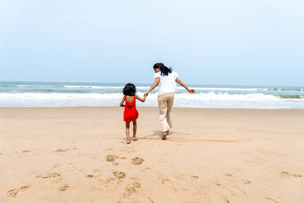 A heartwarming scene of a mother and child walking hand in hand on a tranquil beach, leaving footprints in the sand. The overcast sky adds to the serene backdrop.