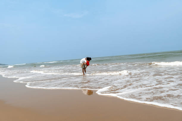 Young South Asian woman in a white sundress stands barefoot in shallow water at twilight, glancing over her shoulder with a warm smile. Gentle waves ripple behind her under a deep blue sky, creating a serene coastal ambiance. Perfect for travel, lifestyle, romance, or evening serenity themes.