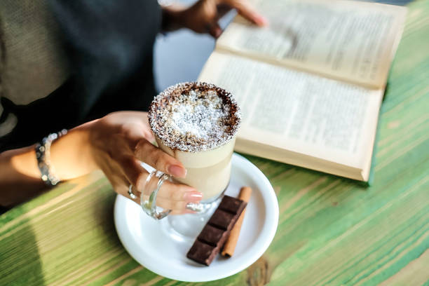 istock Person Holding a Cup of Coffee and Reading a Book at a Table. 2155304586